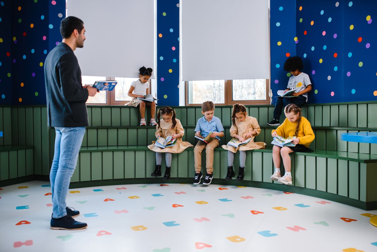 Sample image of children reading books while a teacher stands nearby with a tablet